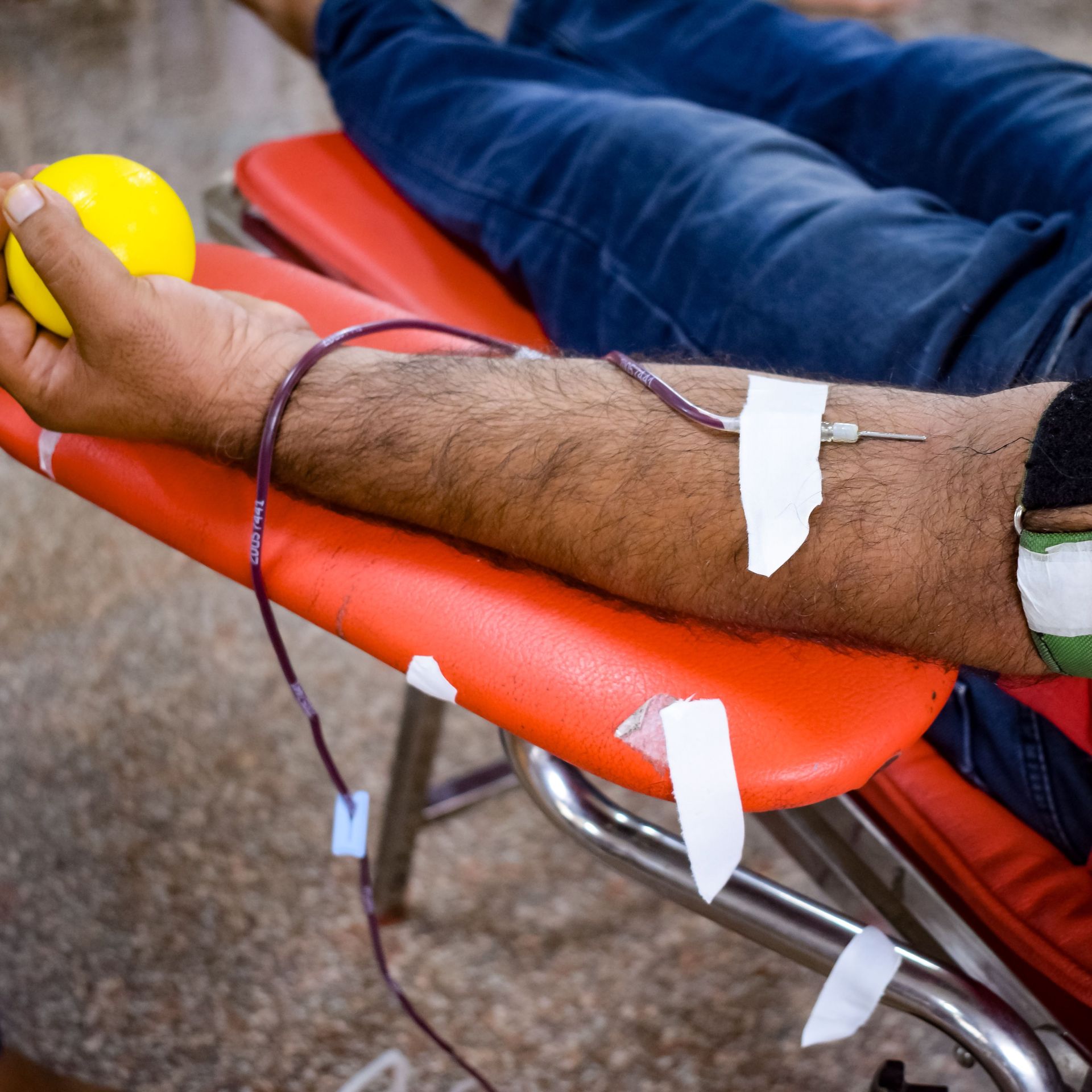 A close-up shot of a man donating blood in a hospital setting, focusing on his arm and equipment.